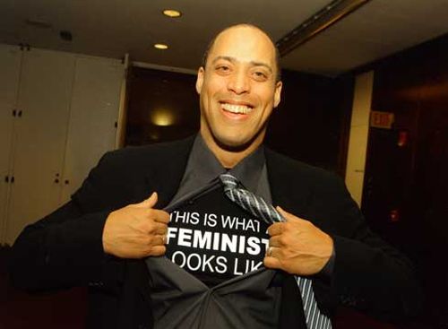 image of Don McPherson, a black man in a jacket and tie, smiling broadly and opening his button-down shirt to reveal a t-shirt underneath reading: 'This is what a FEMINIST looks like.'
