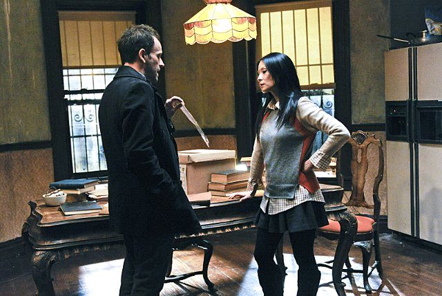 image of Jonny Lee Miller and Lucy Liu standing and chatting while Miller holds out a piece of paper for her observation in an episode of Elementary