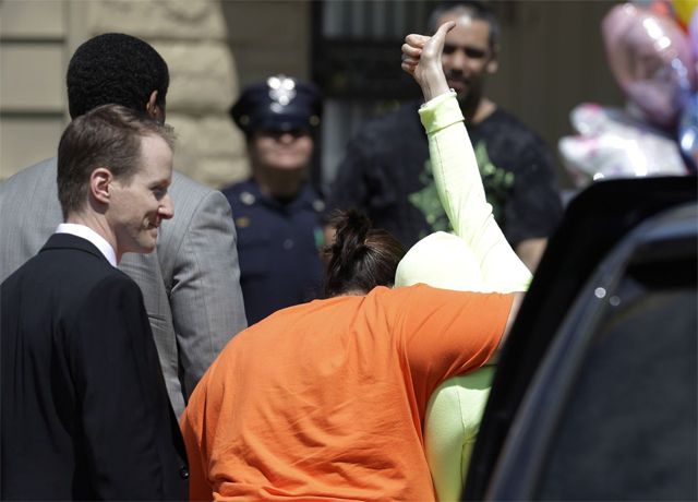 image of a young woman being held as she walks away from the camera, her arm lifted high above her head, giving the thumbs-up