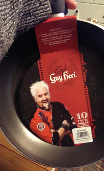 image of my hand holding up a Guy Fieri brand skillet, featuring a picture of Guy Fieri's grinning mug