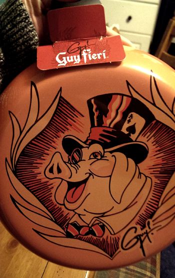 image of the back of the skillet, which is pink, and features a cartoon image of a pig in a top hat and wearing a monocle, with Guy Fieri's signature