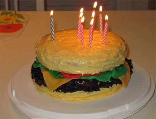 image of a birthday cake in the shape of a cheeseburger, with candles in it