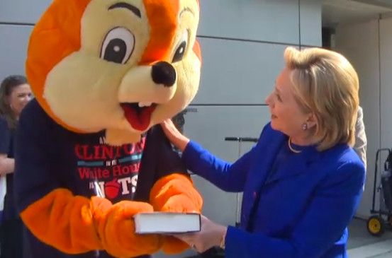 image of Hillary Clinton handing a copy of her book to a person dressed in a squirrel costume and wearing a t-shirt that reads: 'Another Clinton in the White House is NUTS.'