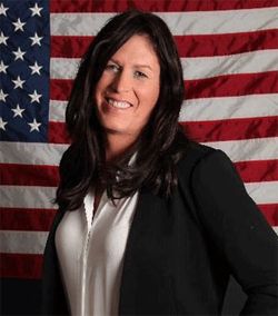 image of a young white woman with long brown hair, standing in front of a US flag