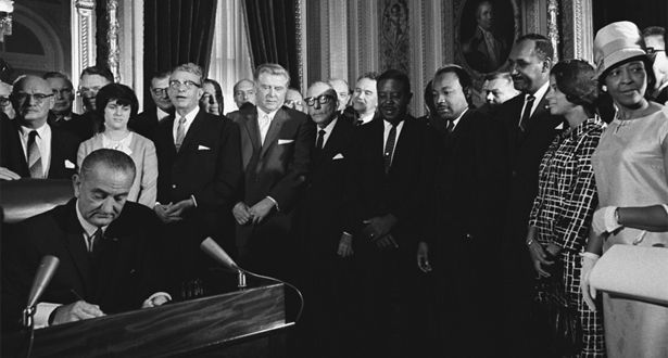 President Lyndon Johnson signs the Voting Rights Act of 1965 into law while a group of people, including Dr. Martin Luther King, Jr., look on