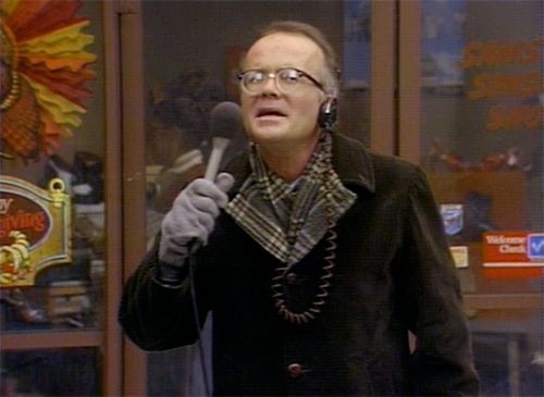 image of the WKRP character Les Nessman, a white man with glasses, reporting from the field