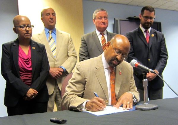 image of Mayor Michael Nutter, a middle-aged black man, signing the bill while flanked by a woman and three men, all of whom appear to be white