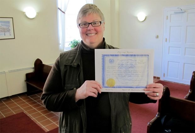 a middle-aged white woman smiles while holding up her marriage license