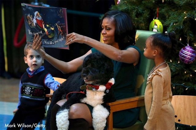 Obama holds the book up over Bo, while the children listen intently