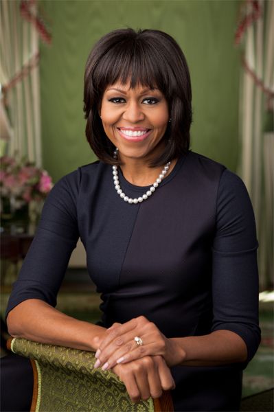 portrait of First Lady Michelle Obama wearing a navy dress with three-quarter-length sleeves as she leans into a green chair