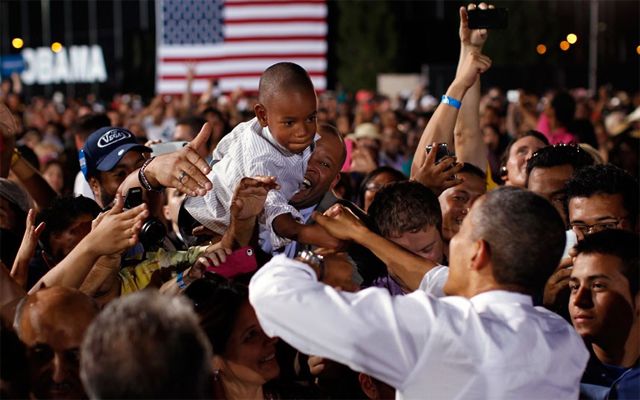 image of a small black boy being raised above a crowd at a campaign event so he can shake hands with President Obama