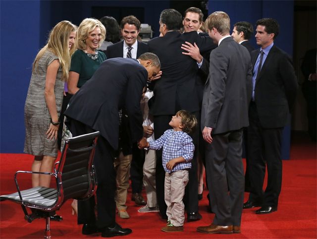 President Obama and a small white boy standing on the edges of a group of people; Obama is leaning over and shaking the boy's hand