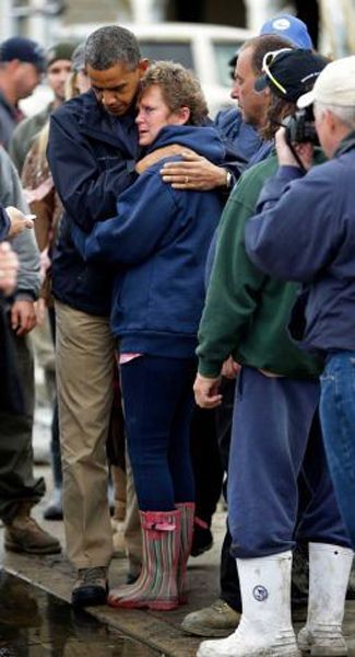 President Obama stands beside an older white woman, hugging her around the shoulders as she hugs him around the waist