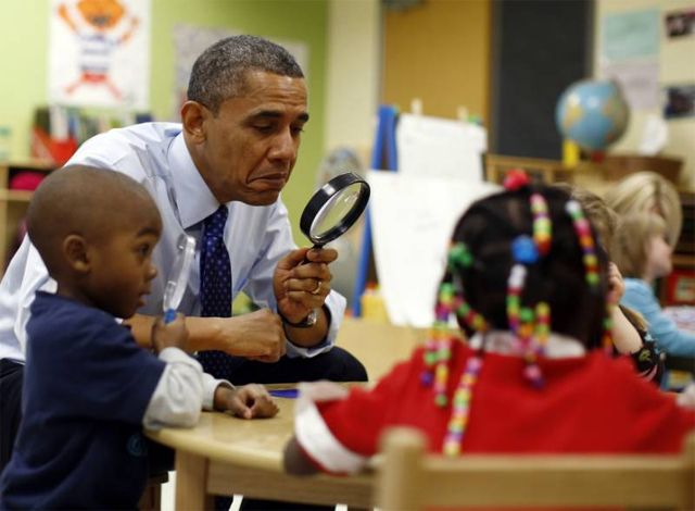 image of President Obama looking through a magnifying glass while sitting at a table with children