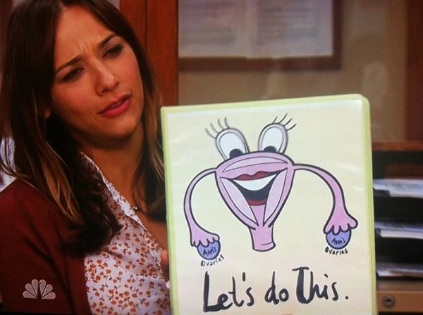 image of Ann Perkins (Rashida Jones) holding up a binder with a smiling uterus cartoon reading LET'S DO THIS