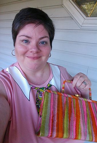 image of me standing on my porch wearing a pink tank top with an appliqué around the neck to mimic a white collar and green patterned scarf, and holding a vintage purse with pink, orange, and green stripes
