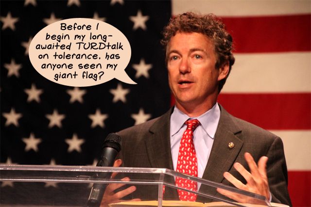 image of Rand Paul speaking in front of a giant US flag, to which I have added text reading: 'Before I begin my long-awaited TURDtalk on tolerance, has anyone seen my giant flag?'