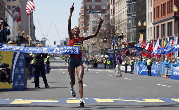 image of Rita Jeptoo, a thin black woman, crossing the finish line with her arms in the air, pointing upwards