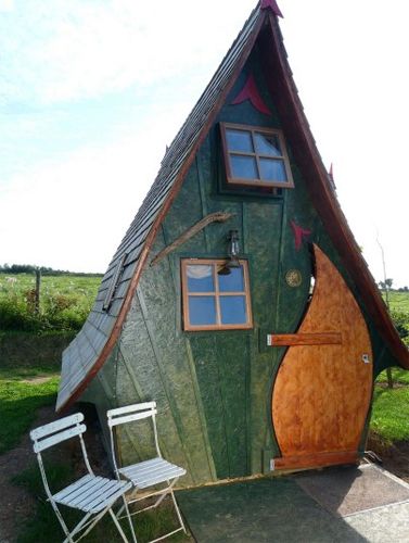 image of an inverted teardrop-shaped shed, with lots of odd angles and lines, with two white chairs sitting outside