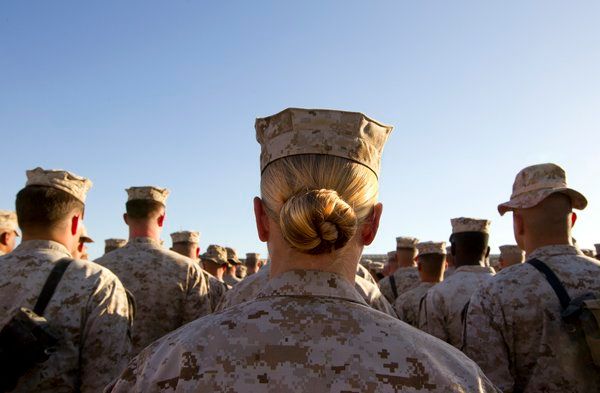 image of the backs of uniformed military personnel; a woman with her hair tied into a bun stands at the back