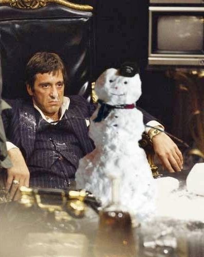 image of Al Pacino scowling at a dek covered in cocaine; his face and the front of his clothes are covered in cocaine; there is a photoshopped snowman sitting on his desk, grinning