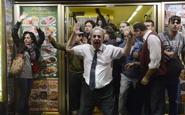 image of protestors in Spain standing the doorway of a shop, raising their hands in the air and shouting