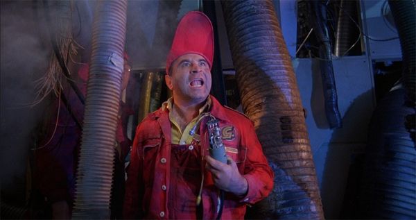 screen cap from the movie 'Brazil' with Bob Hoskins as Spoor, dressed in a red jumpsuit and oversized red cap