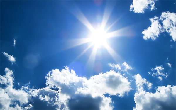 image of a sunny blue sky with a brightly shining sun and fluffy white clouds