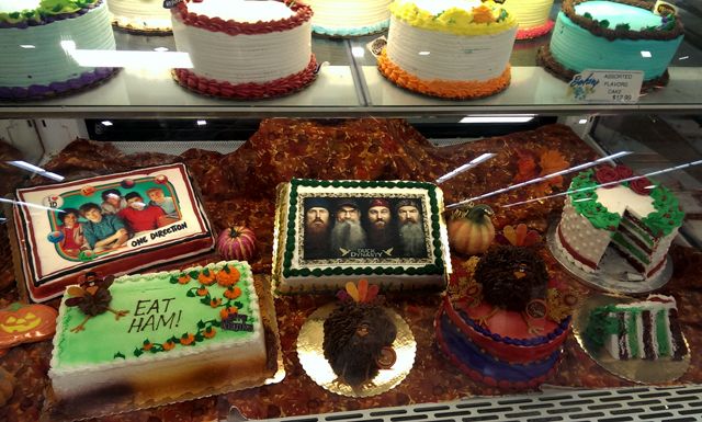 image of a Thanksgiving-themed cake display featuring a Duck Dynasty cake, a One Direction cake, and a cake on which is handwritten in icing EAT HAM!