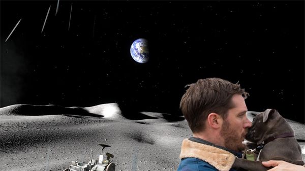 actor Tom Hardy kisses a grey pit bull puppy on the muzzle on the surface of the moon, with the Earth in the background