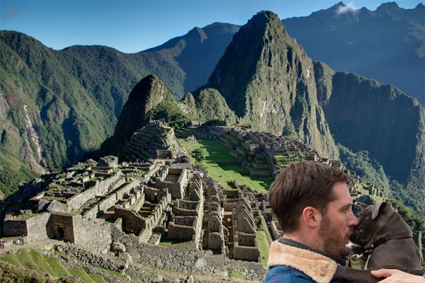 actor Tom Hardy kisses a grey pit bull puppy on the muzzle in front of the Historic Sanctuary of Machu Picchu
