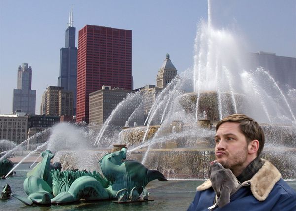 image of actor Tom Hardy and a grey pit bull puppy who is licking Tom's chin while peeking its head out of his coat