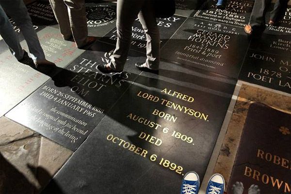 image of the floor at Poets' Corner in Westminster Abbey, focusing in on the marker for Alfred Lord Tennyson; in the bottom righthand corner of the image, the top of a pair of blue Converse sneakers and a pair of grey dog paws are visible