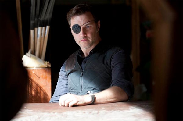 image of Governor Cyclops (David Morrissey) sitting at a table in a dimly lit barn, looking grim