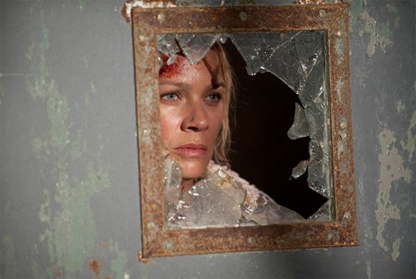 image of Andrea peeking through a broken window in an abandoned building
