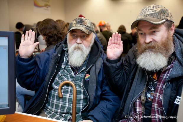 image of two late middle-aged men with long beards holding up their hands to swear to honesty while applying for a marriage license