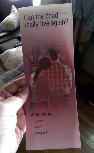 image of my hand holding a flyer featuring a drawing of a straight white couple from behind, gazing at a wall of family photos, accompanied by text reading: 'Can the dead really live again? Would you say... -yes? -no? -maybe?'