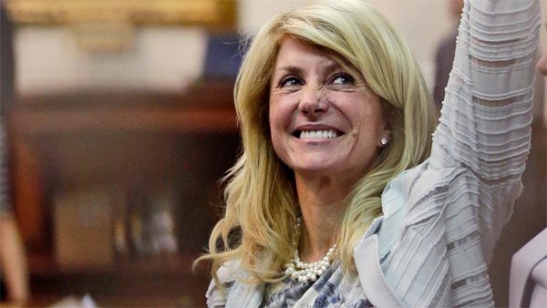 image of Texas State Senator Wendy Davis, a white middle-aged woman with blonde hair, smiling and lifting her arm into the air during yesterday's filibuster