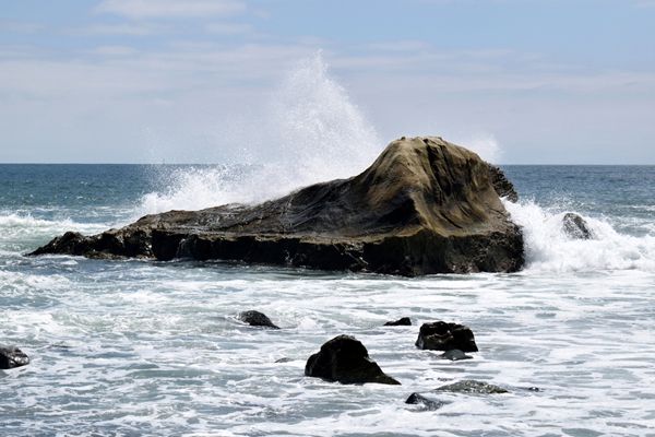 A wave splashes against a large rock off the shore of a beach in Dana Point, CA...on April 20, 2019.