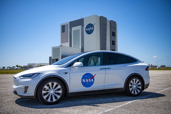 The Tesla Model X that astronauts will ride in on launch day is displayed with Kennedy Space Center's Vehicle Assembly Building in the background.